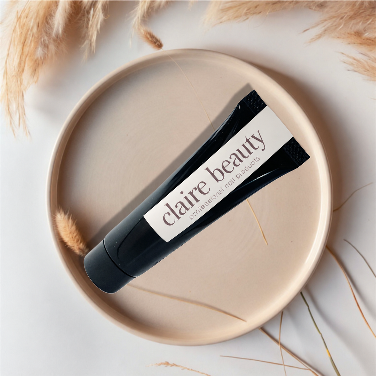 Schwarze claire beauty Press On Glue Gel Tube auf einer beigen Schale mit Trockenblumen